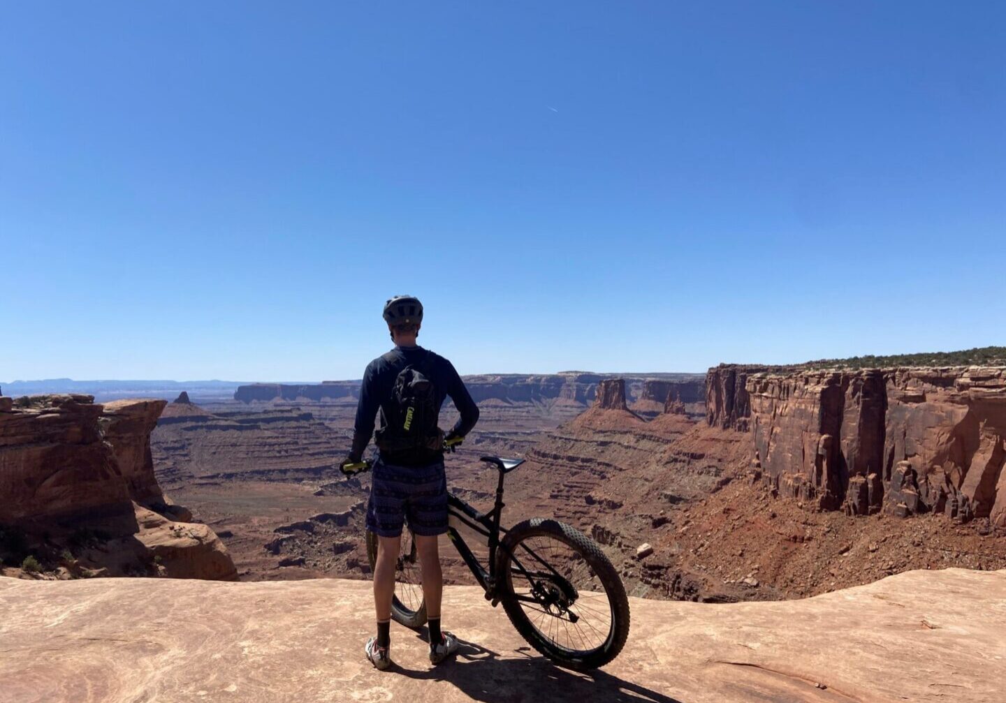 Person with bicycle overlooking a vast canyon landscape under clear blue sky.