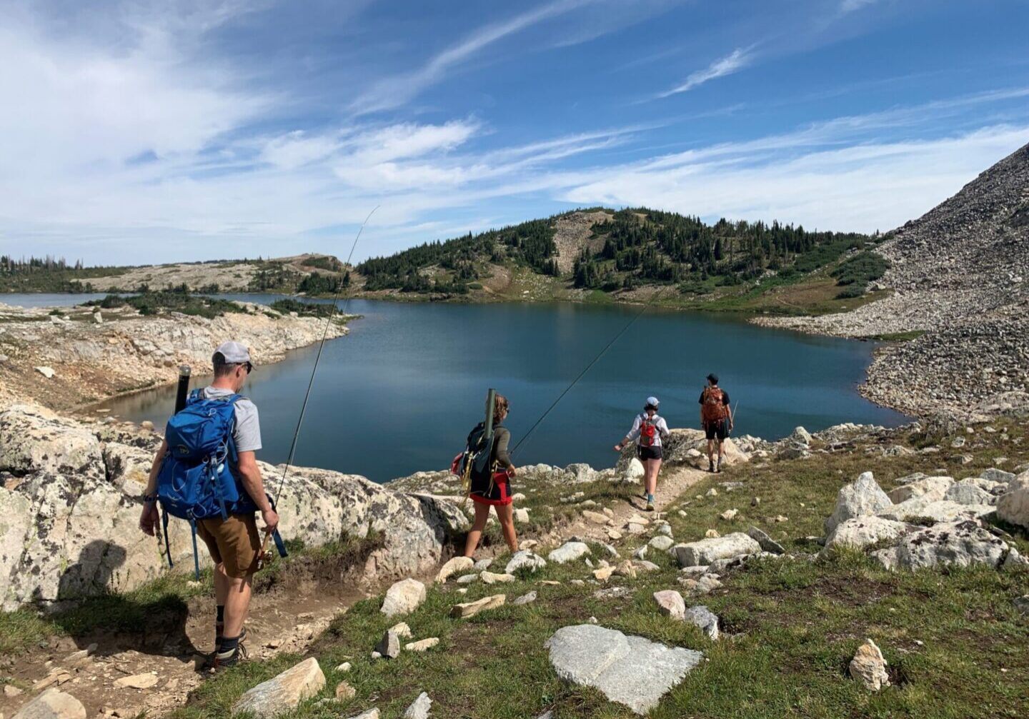 Hikers exploring rocky terrain near a serene lake under a blue sky.