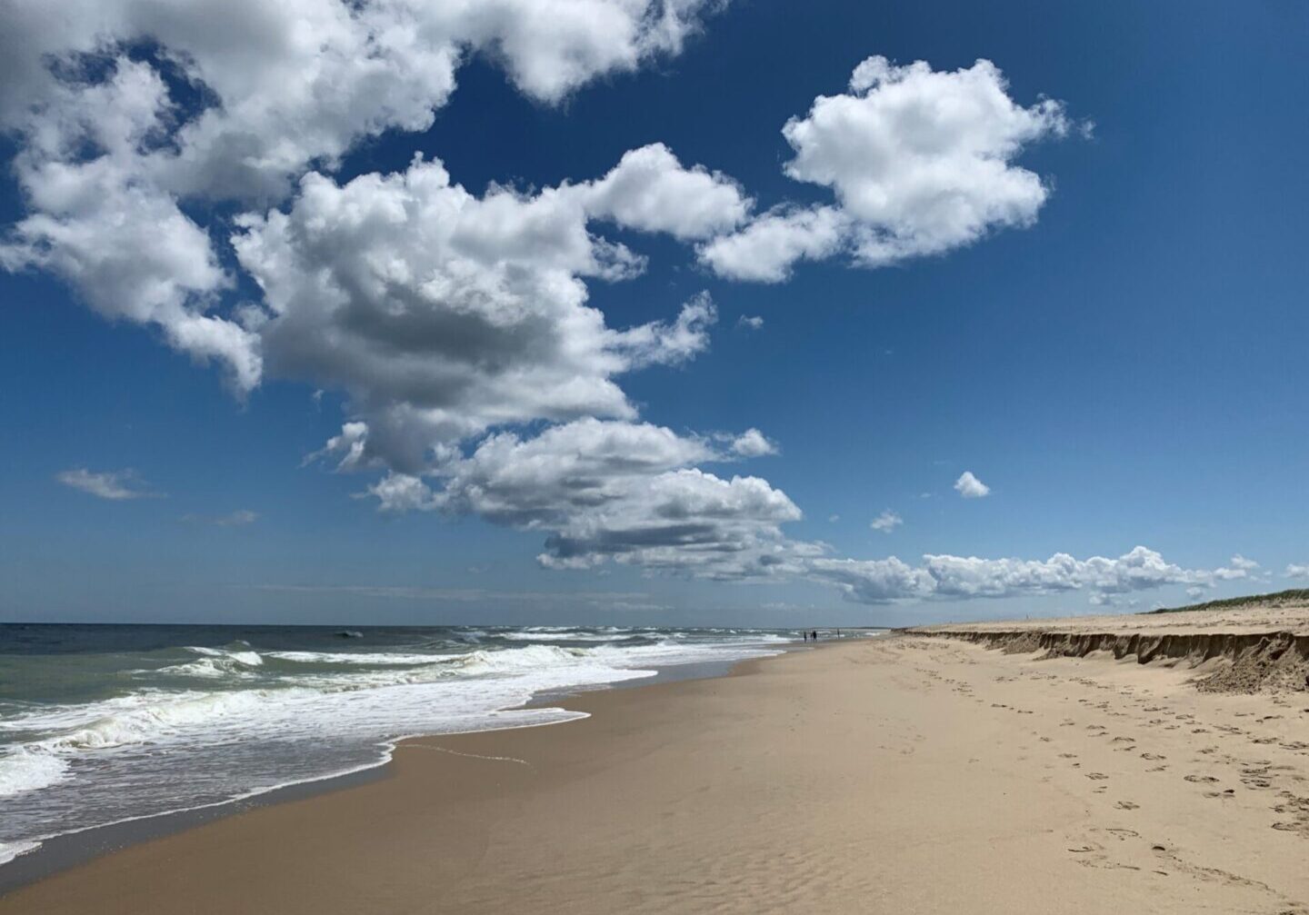 A beach with waves and clouds in the sky.