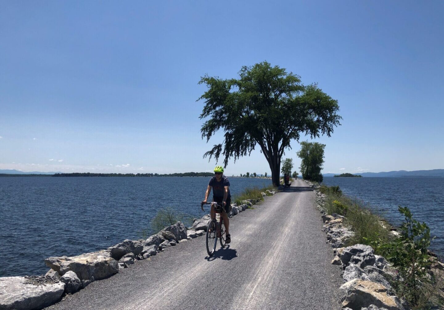 A person riding a bike on the side of a road near water.