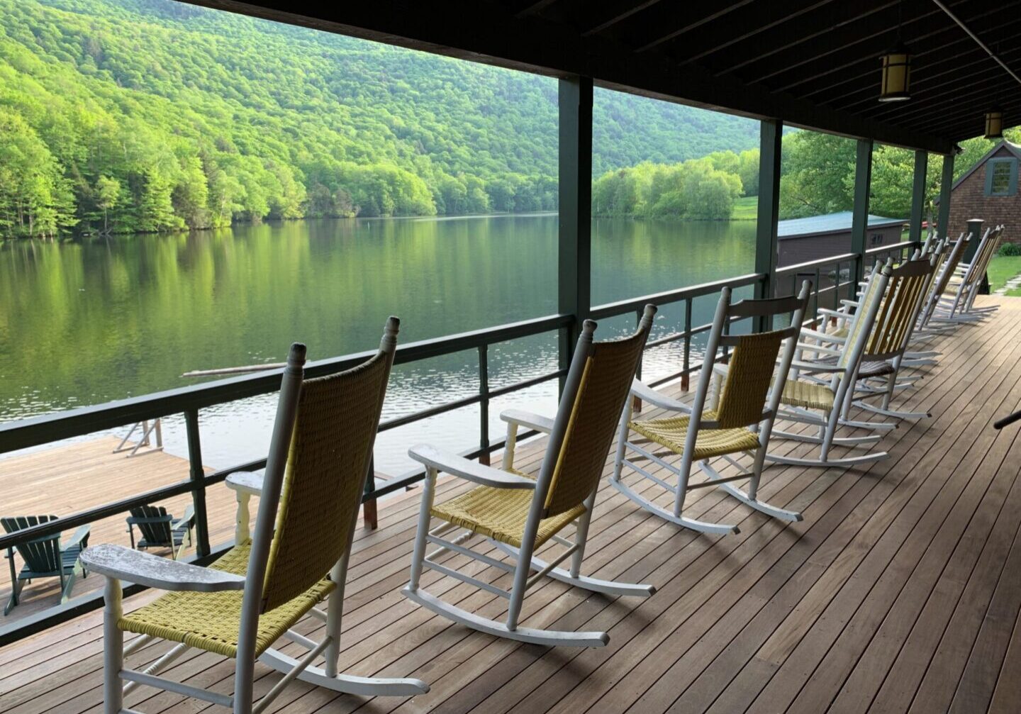 A row of rocking chairs on the deck overlooking a lake.